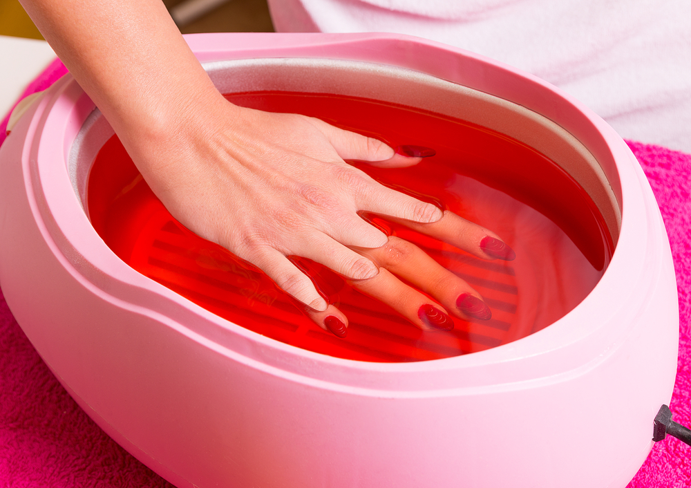 Female hand and orange paraffin wax in bowl. Manicure and skincare. Woman girl in beauty spa salon.